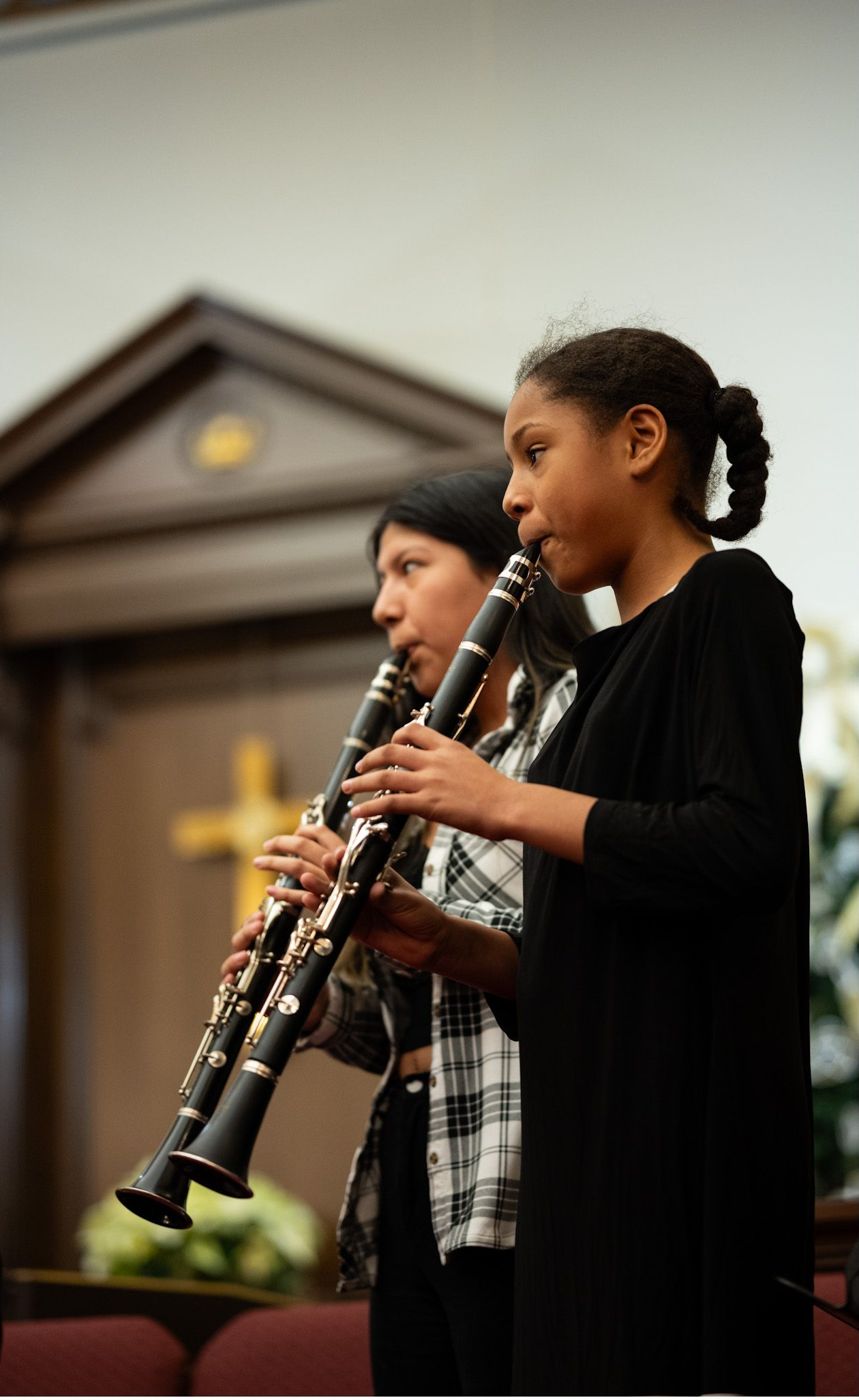 Young musician playing a clarinet during a church performance, with another player blurred in the background