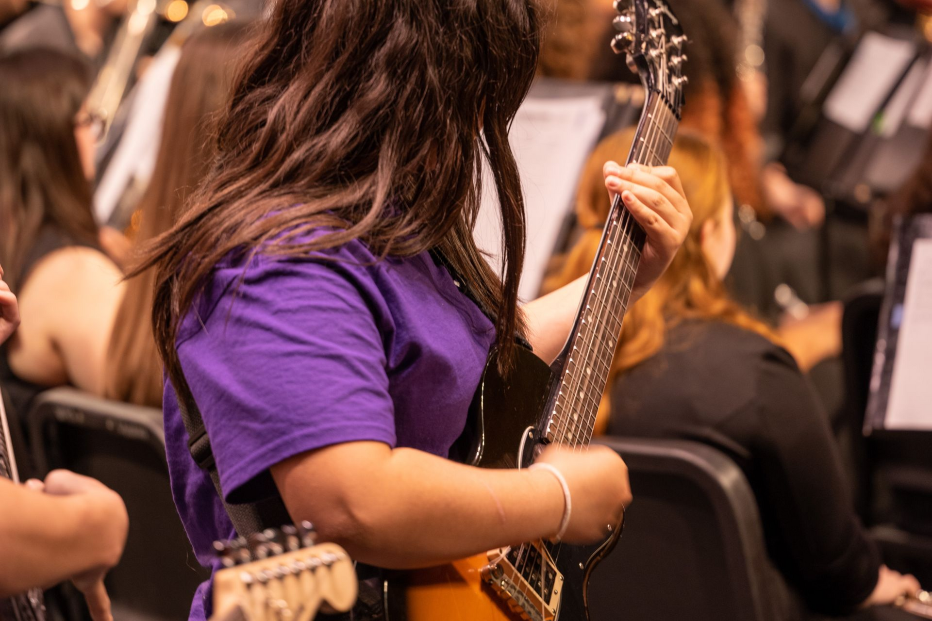 Musician in purple shirt holding an electric guitar in a crowded performance setting