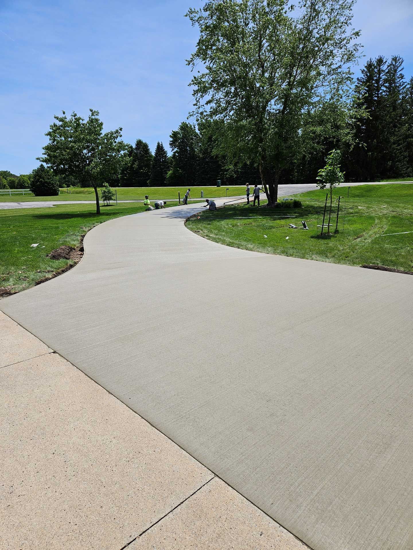 A concrete walkway going through a park with trees on both sides.