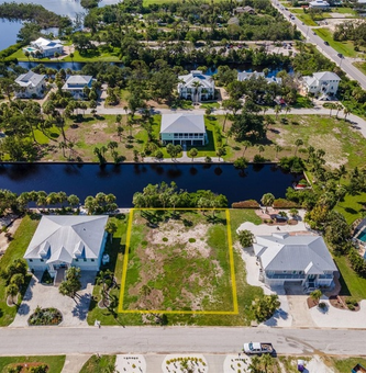 Aerial view of canal-side homes and vacant lots in a sunny suburban neighborhood