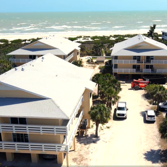 Aerial view of beachfront cottages with white roofs and parked vehicles beside the ocean