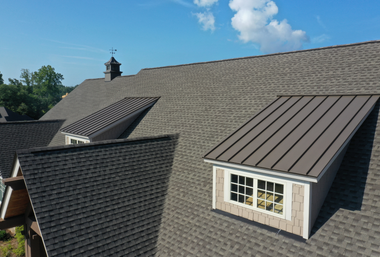 Roof with gray shingles and two dormer windows under a blue sky