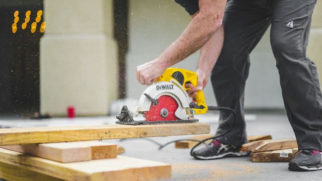 Worker cutting wood with a circular saw on a construction site, with sawdust flying.