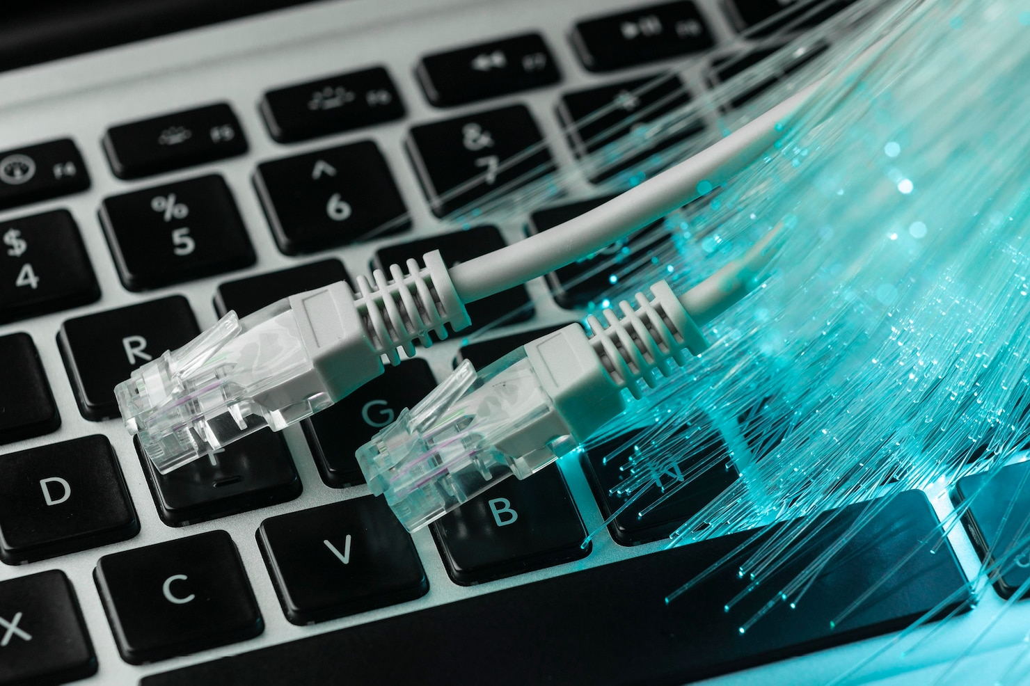 A close up of a laptop keyboard with ethernet cables coming out of it.
