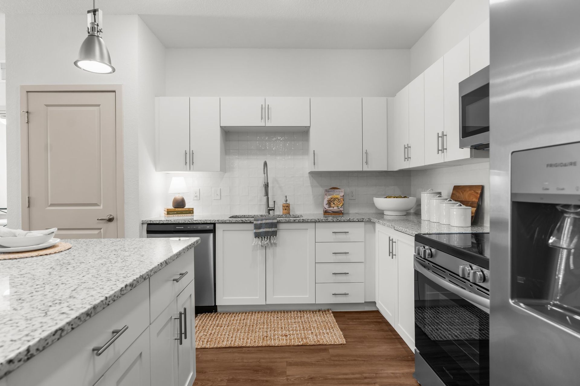 Bright white kitchen with granite countertops, stainless steel appliances, and wood floors.