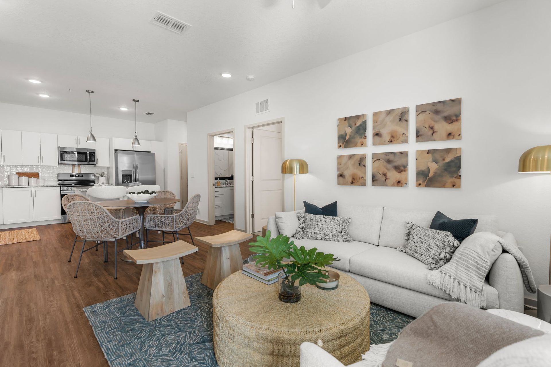 Open-concept living space: white walls, wooden floors, kitchen, living room with sofa, rug, coffee table, and art.