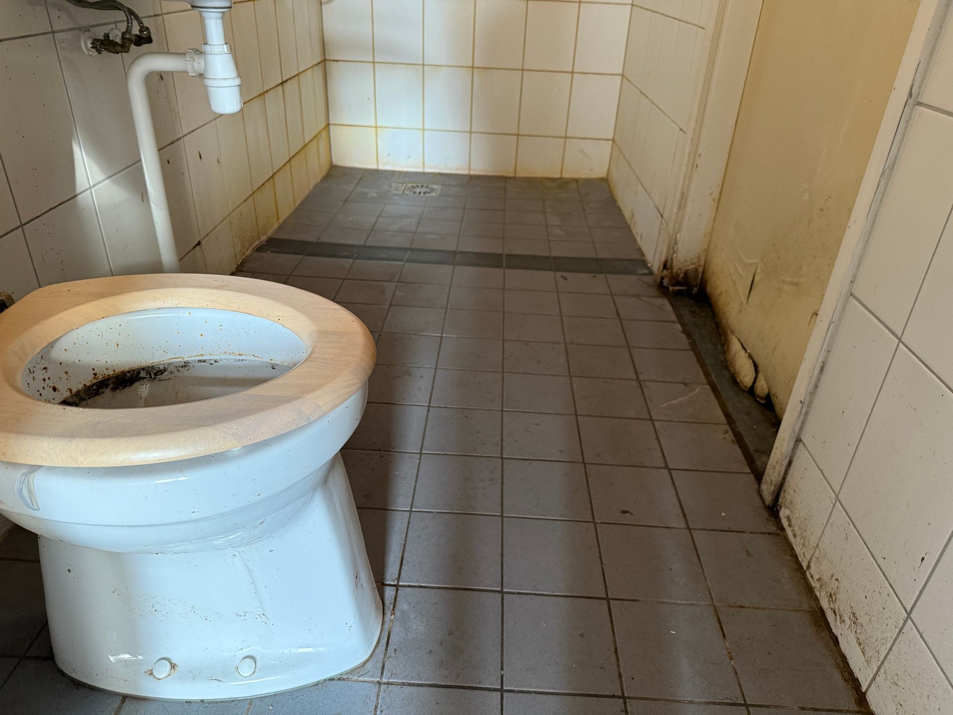 Een smerig openbaar toilet met een bevlekte wc-pot, betegelde muren en vloer.