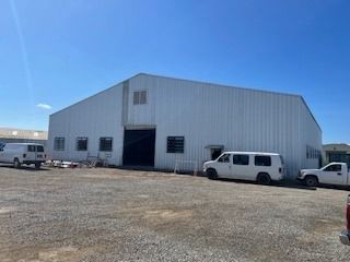 White industrial building with parked vans and a truck against a blue sky.