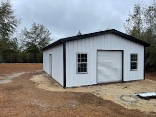 White metal garage with black trim, roll-up door, two windows, and side door, outdoors in a field.