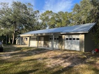 A tan building with a metal roof and several garage doors sits among trees on a sunny day.