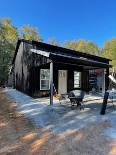 Black-sided building with white door and windows under construction on a sunny day. Wheelbarrow sits outside.