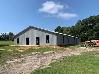 Gray metal building under construction on a grassy lot, with a blue sky and few clouds in the background.