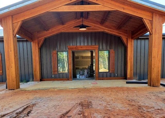 Wooden-framed building exterior with a covered entryway, light fixture, and two tall windows; gray siding, brown trim.