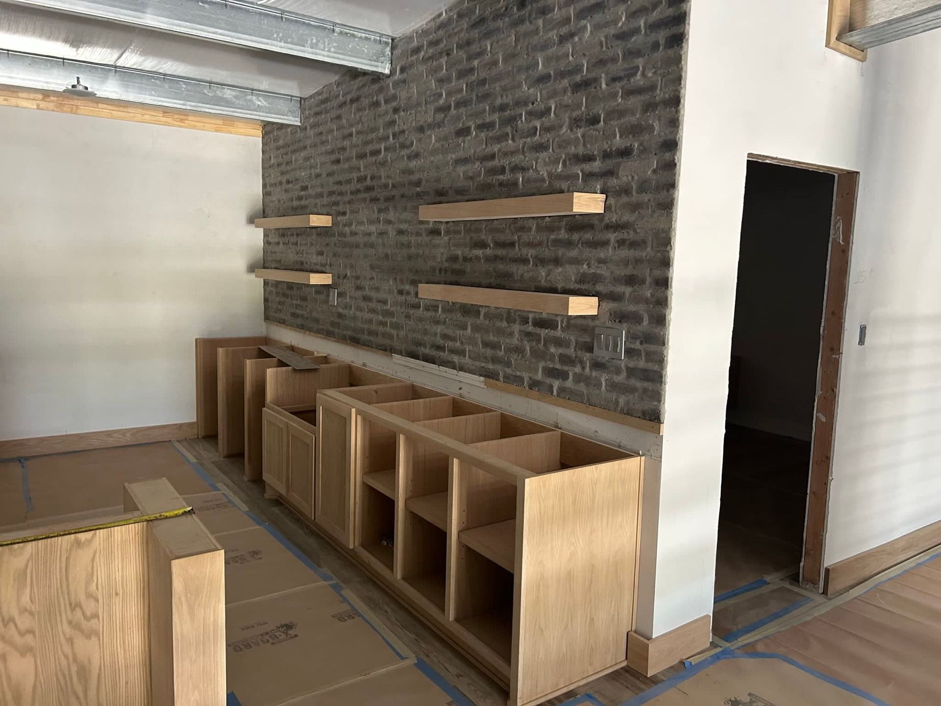 Interior under construction; brick wall with wood shelves and cabinetry.
