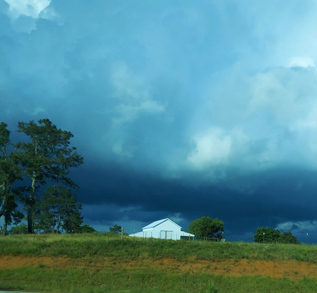 Stormy sky over a white building and green field with trees.