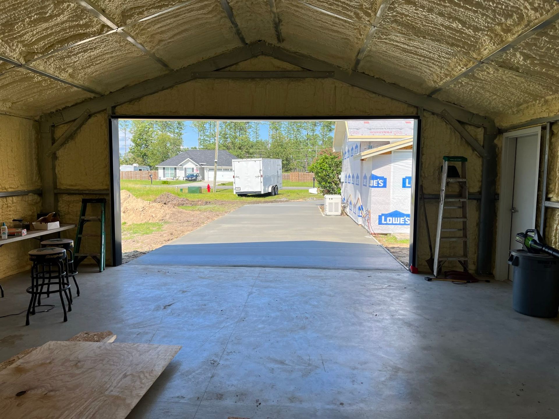 Interior view of a newly constructed garage with the door open, showing a concrete driveway, lawn, and houses