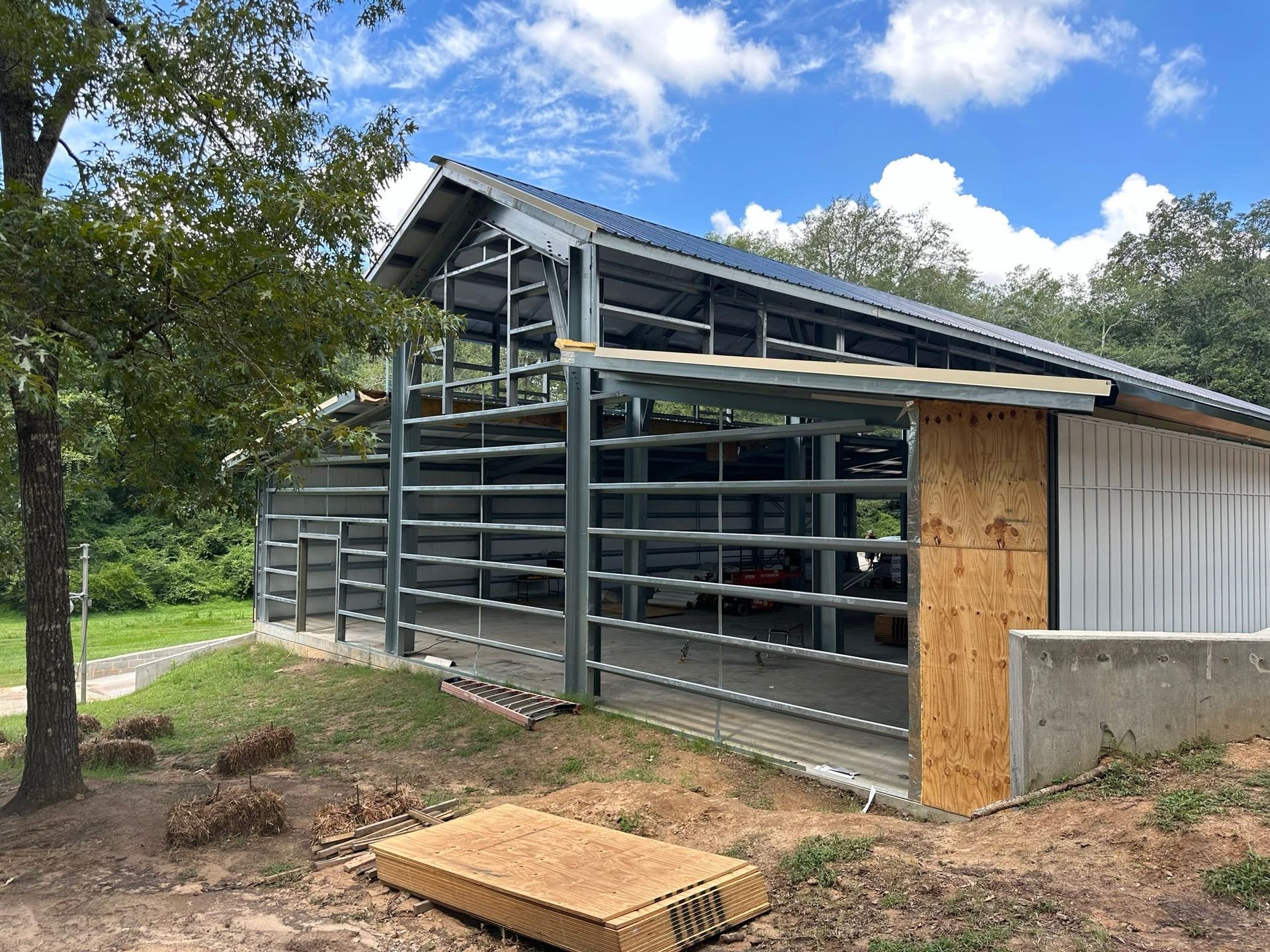 Steel frame barn under construction outdoors on a grassy hill, with trees in the background