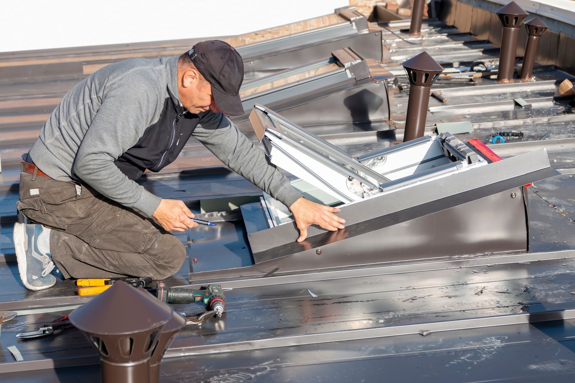 Worker kneeling on a rooftop, installing a metal skylight or vent panel.