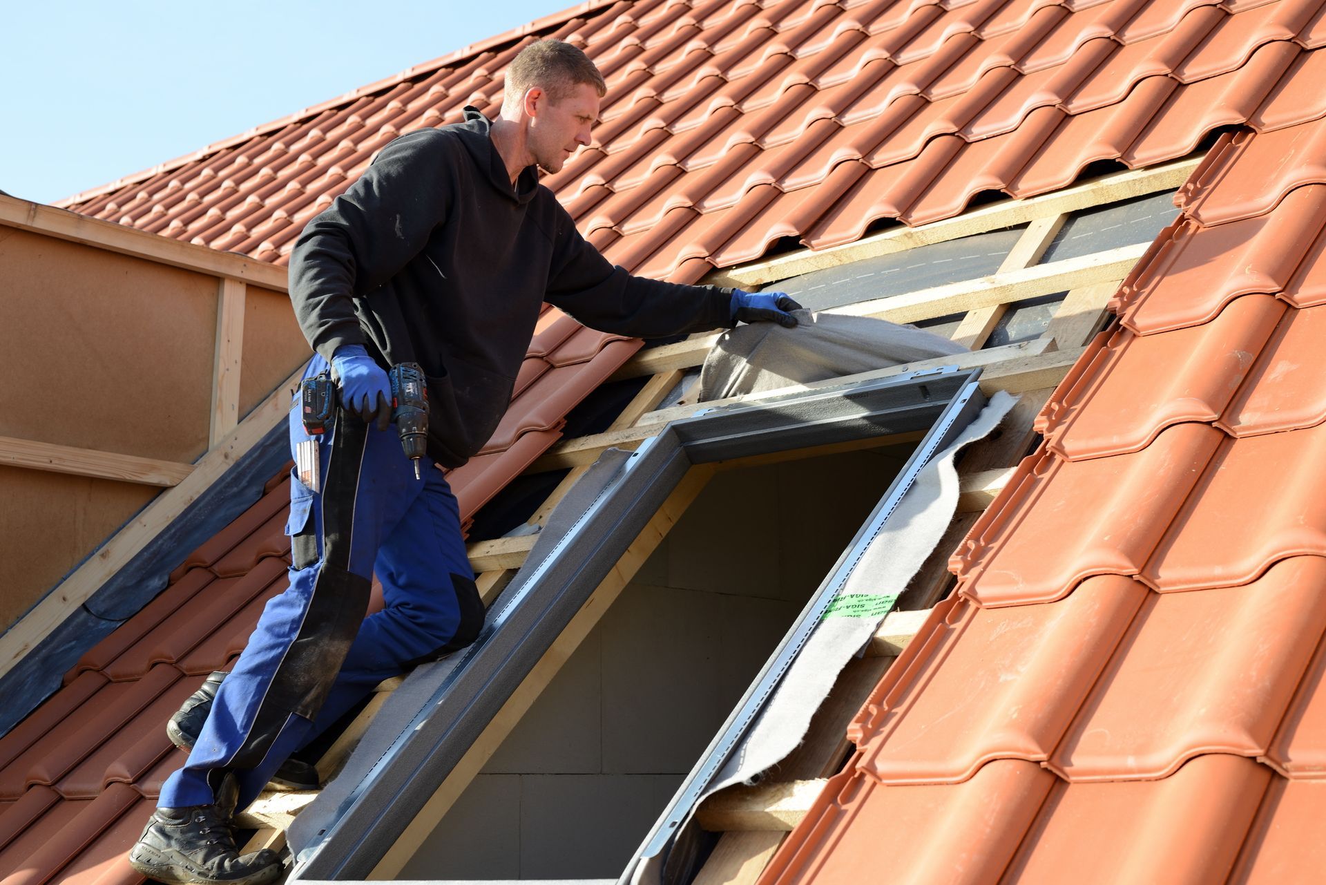 Worker installing a skylight on a tiled roof with tools and blue gloves