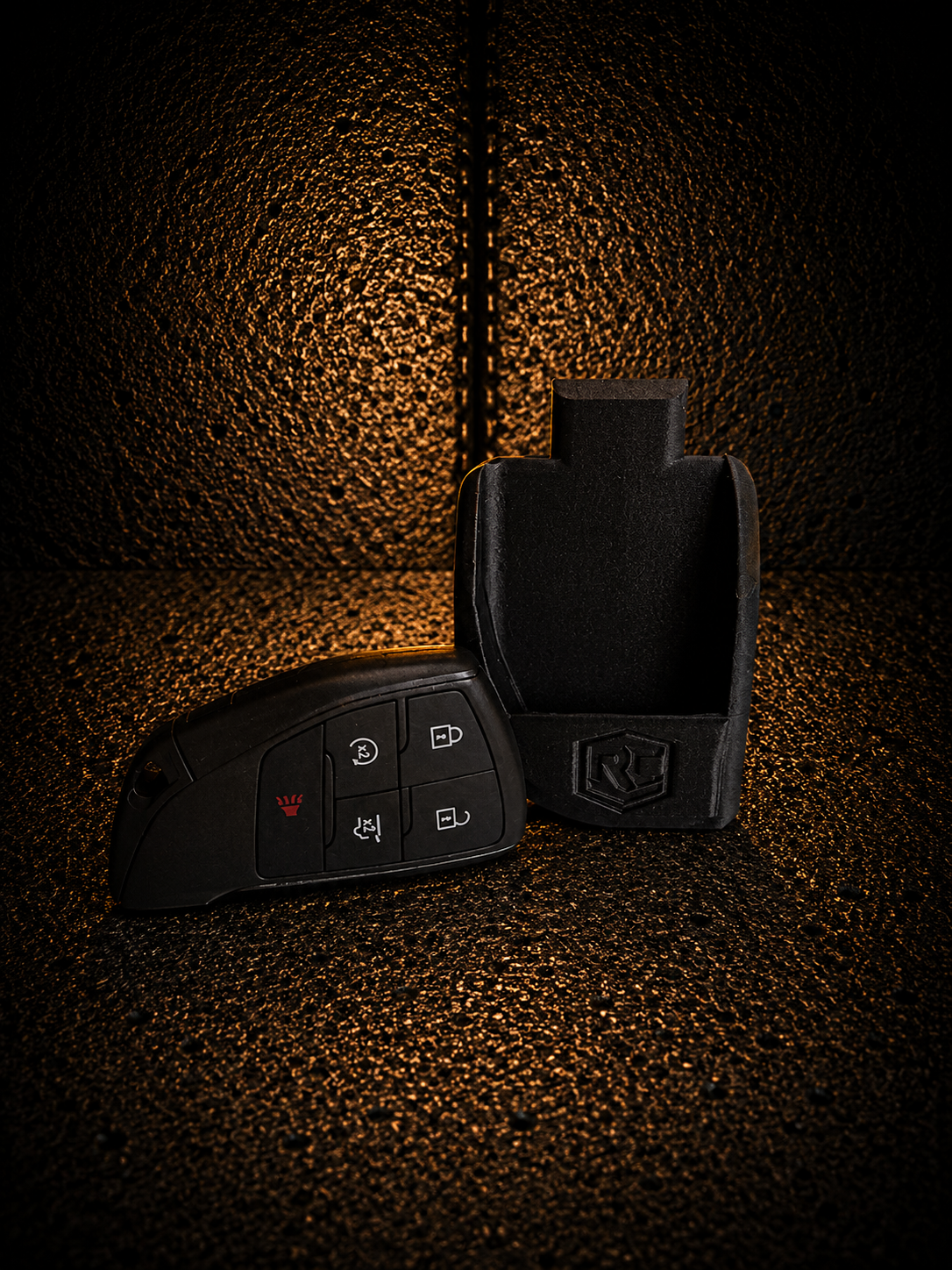 Black car key fob and black key pouch on a textured orange-lit background