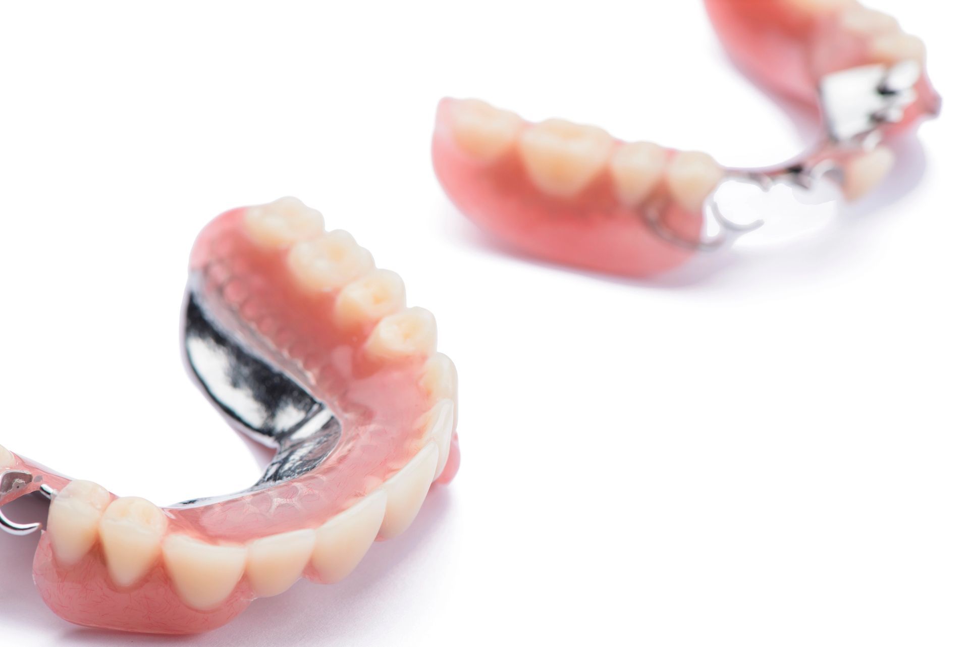 Par de dentaduras postizas removibles rosas y blancas sobre un fondo blanco.