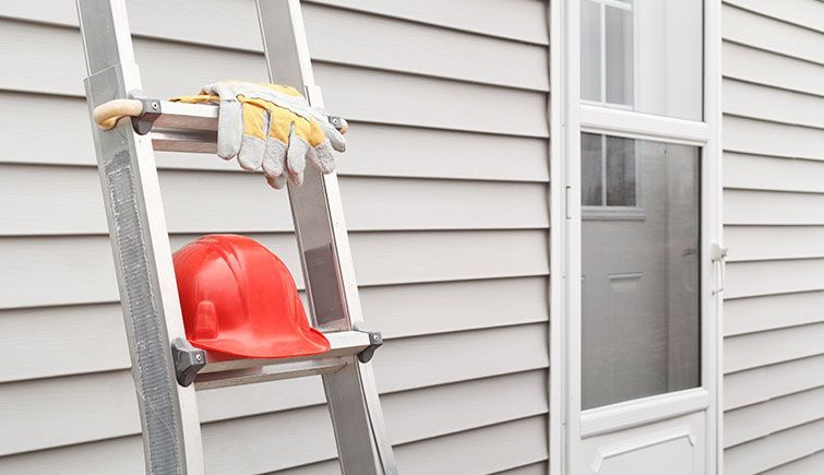 A ladder with a hard hat and gloves on it is leaning against a house.