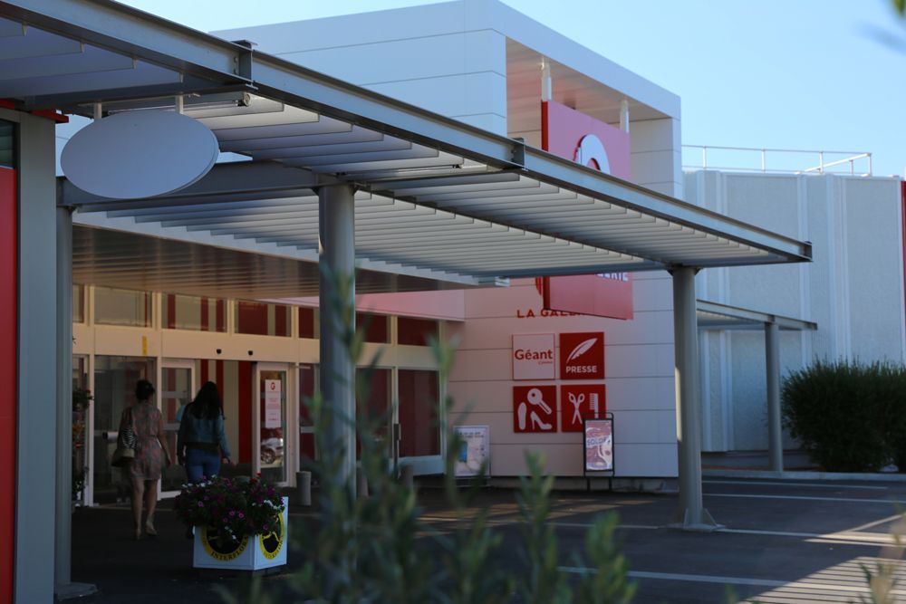 Extérieur d'un magasin moderne avec un auvent au-dessus de l'entrée. Des clients entrent.