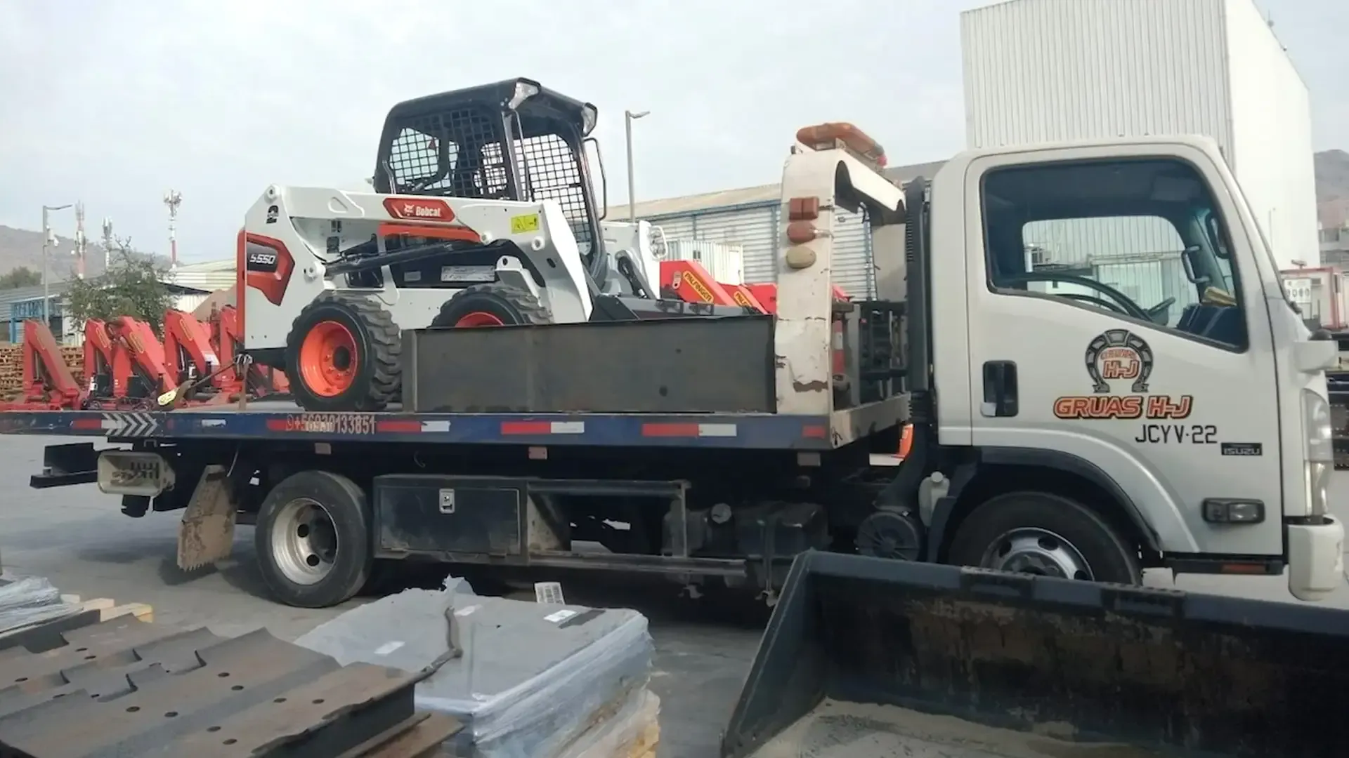 Una minicargadora Bobcat blanca cargada sobre una grúa de plataforma en un área de almacenamiento industrial o al aire libre.