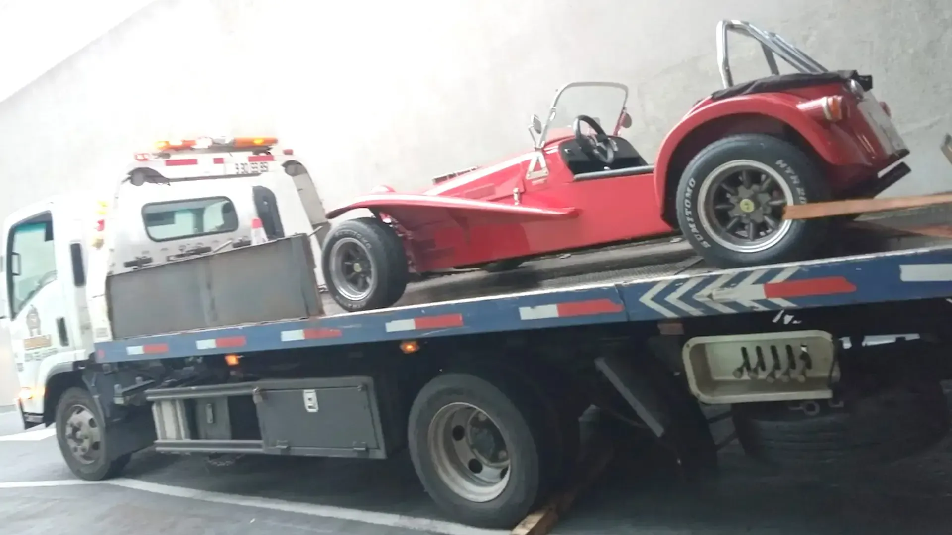 Un deportivo roadster rojo de estilo clásico subido a la plataforma de una grúa blanca.