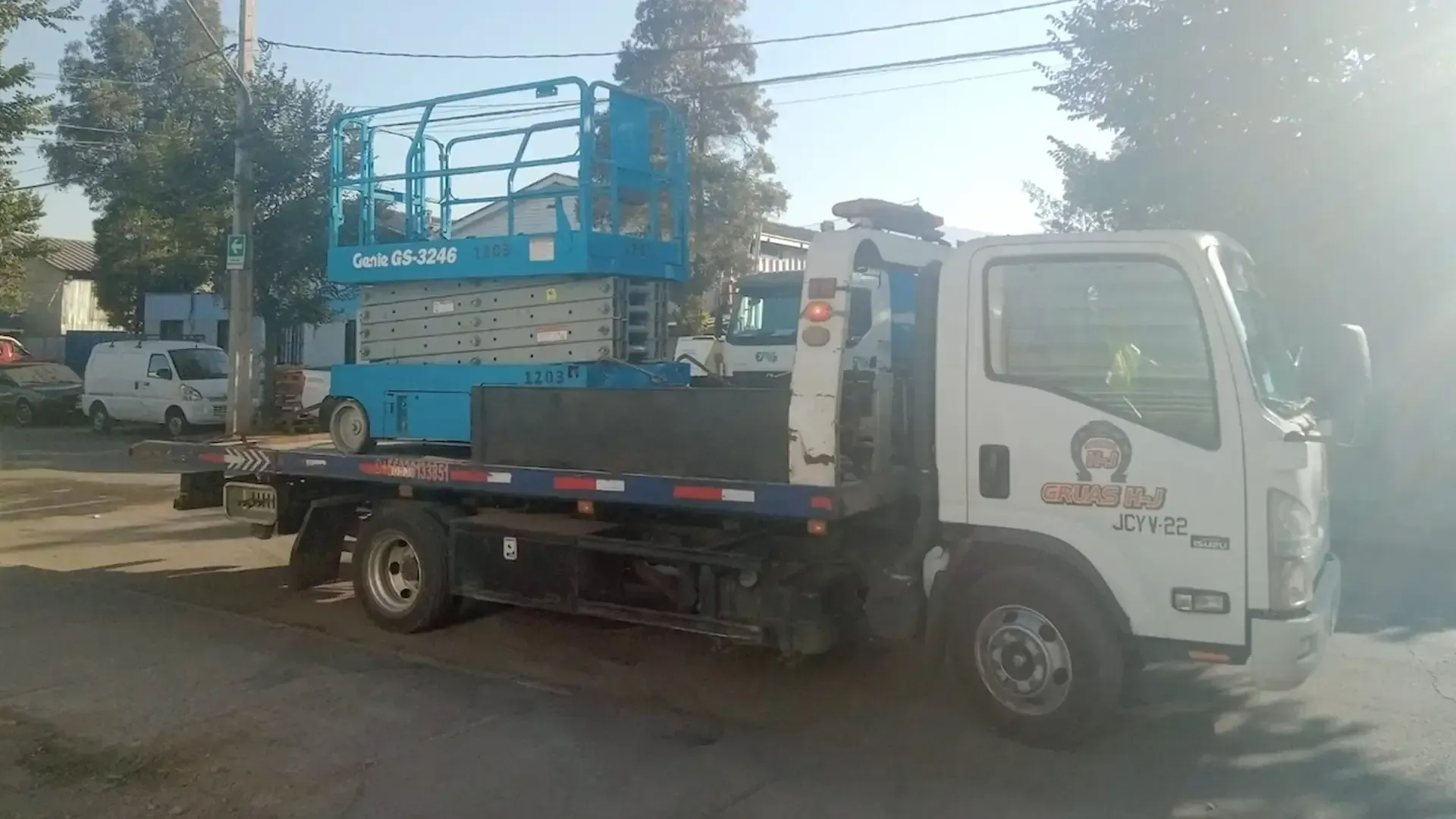 Una grúa de plataforma con una plataforma elevadora de tijera azul estacionada en una calle durante el día.
