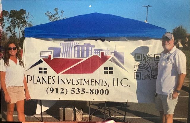 Two people standing in front of a sign for planes investments llc