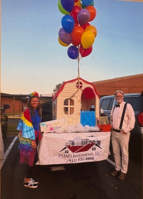 A man and a woman are standing in front of a playhouse with balloons hanging from it