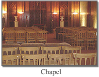 Empty chapel with rows of wooden chairs and warm wall sconces at the front
