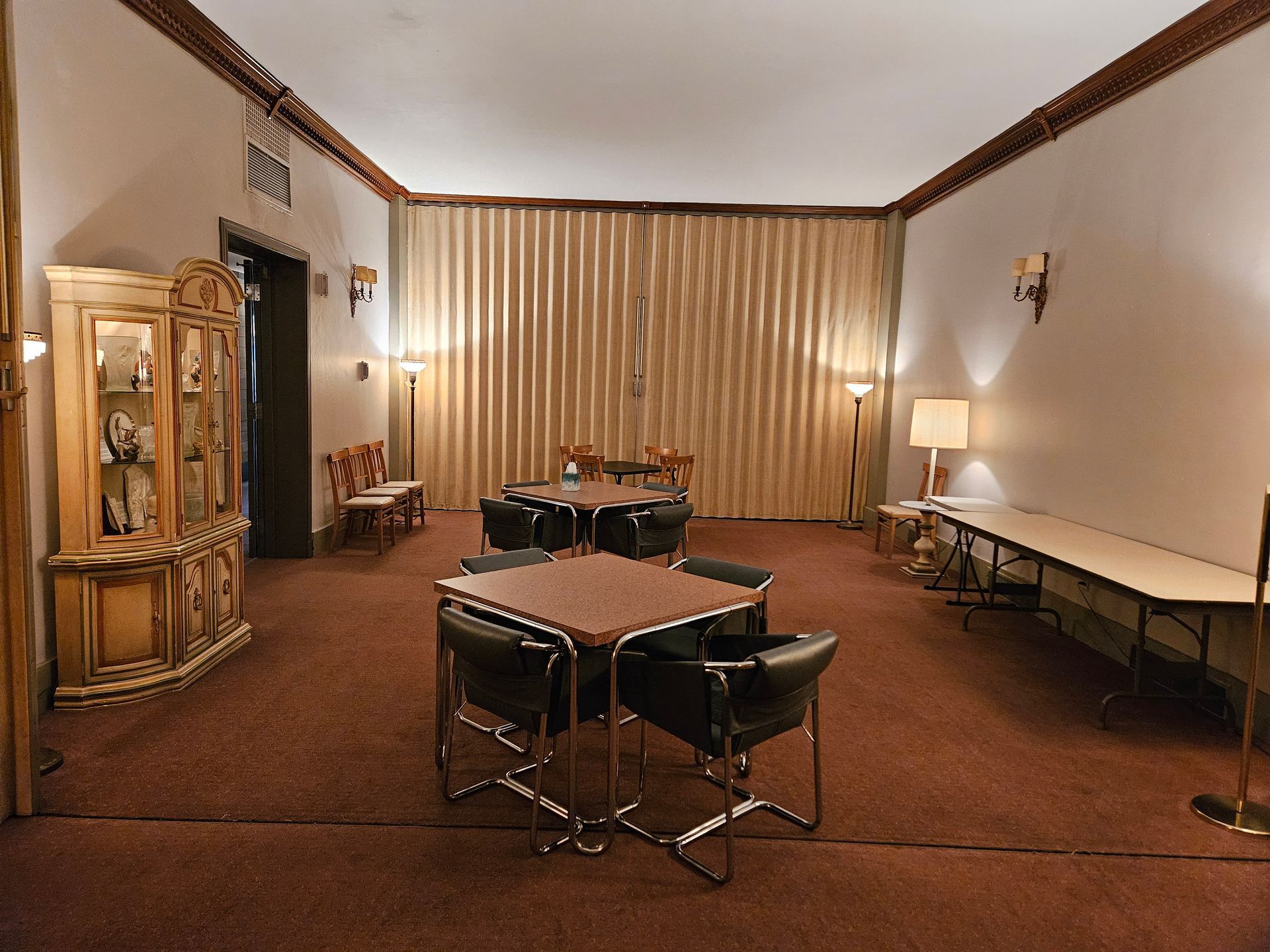 Quiet lounge with a drum set, chairs, long table, lamp, and curtains on brown carpet