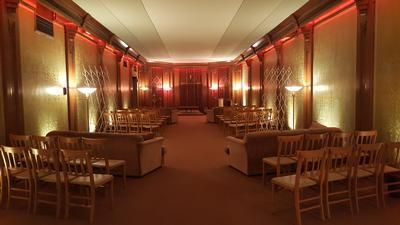Warmly lit banquet hall with rows of empty wooden chairs and tables along the walls