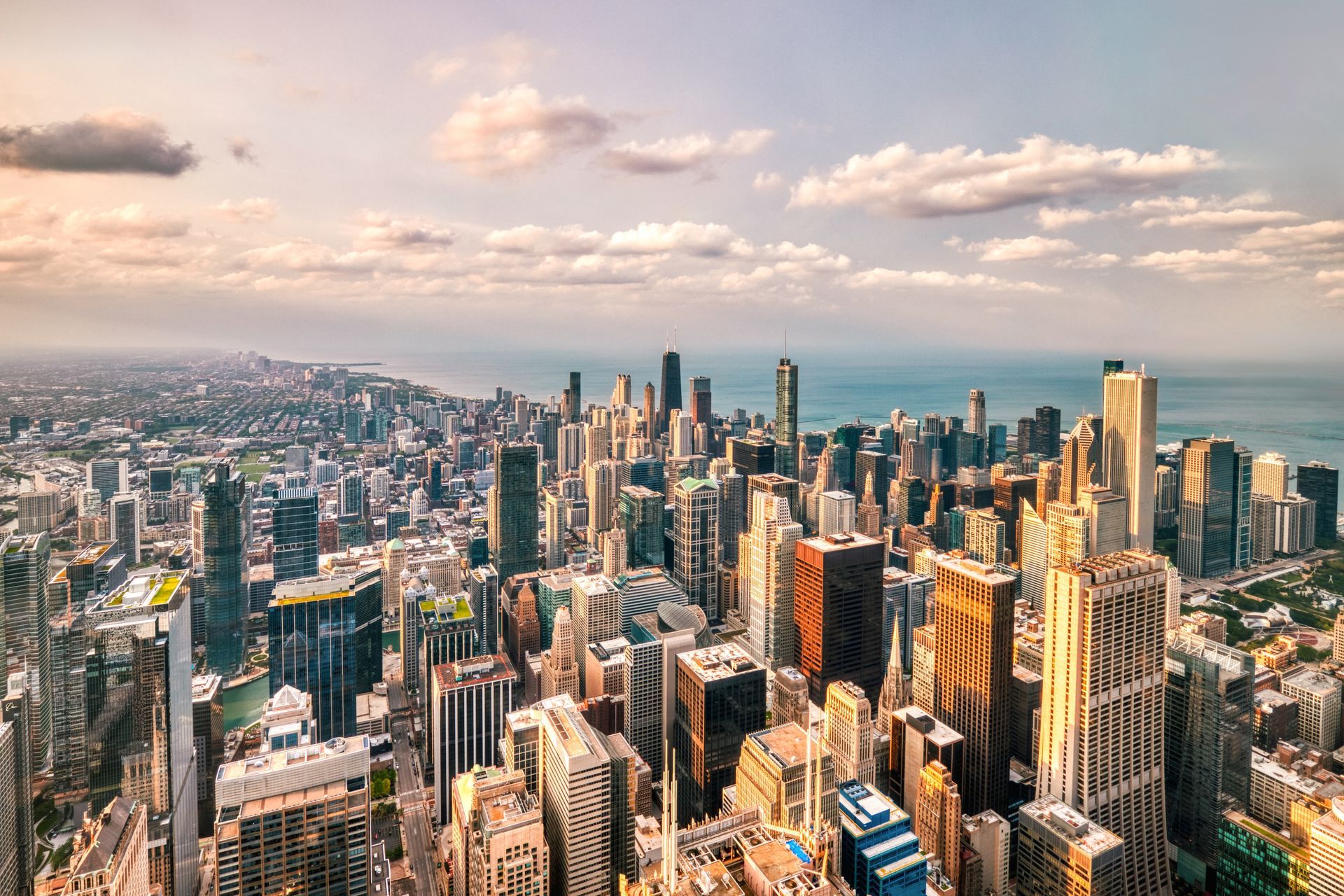 Aerial view of a dense city skyline with tall skyscrapers at sunset under a cloudy sky