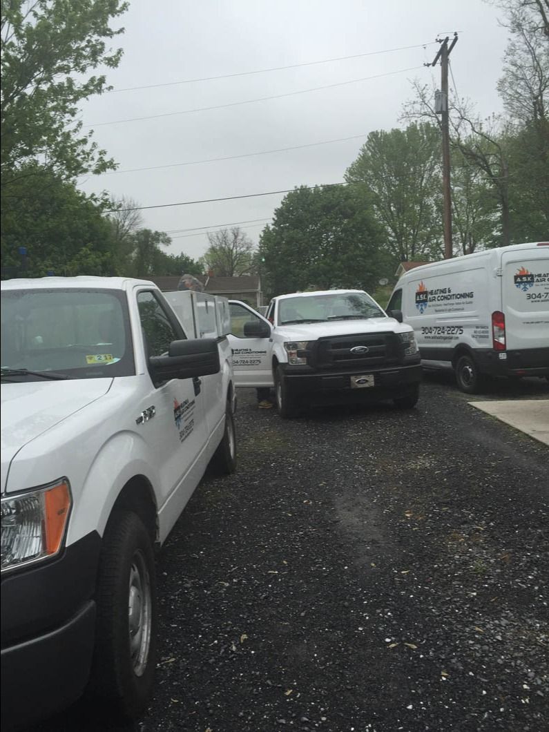 Several white work vans and a black truck parked on a wet gravel lot under cloudy skies