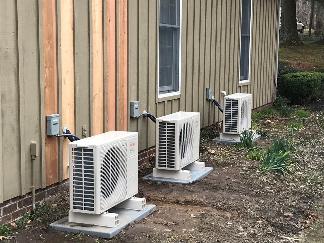Three outdoor air conditioning units beside a beige building wall