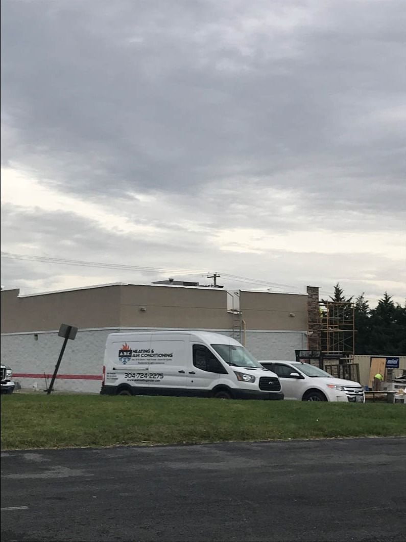 White service van and car parked in front of a large building under a cloudy sky.