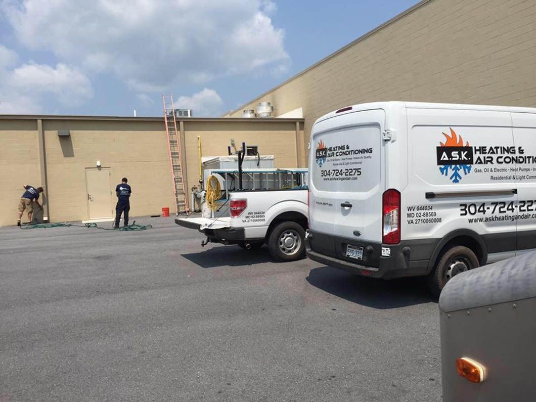 Two utility trucks parked by a beige building, with a worker and ladder in an industrial lot.