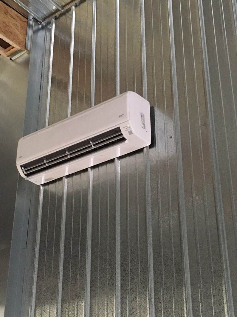 Wall-mounted white air conditioner on a corrugated metal wall.