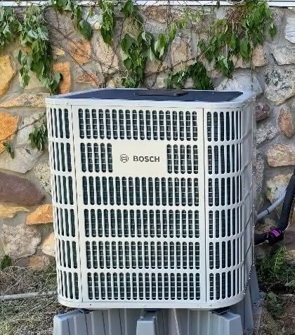 Outdoor HVAC unit beside house with a pink insulated cover on top and plants nearby