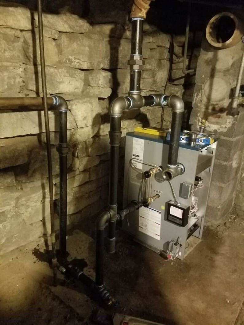 Basement boiler and furnace unit beside stone foundation walls and exposed pipes