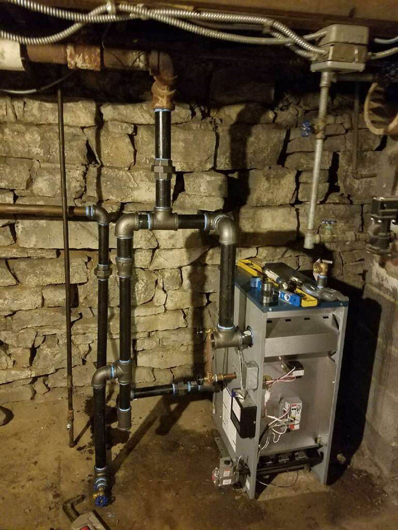 Basement wall with exposed plumbing pipes and a utility boiler or water heater unit.