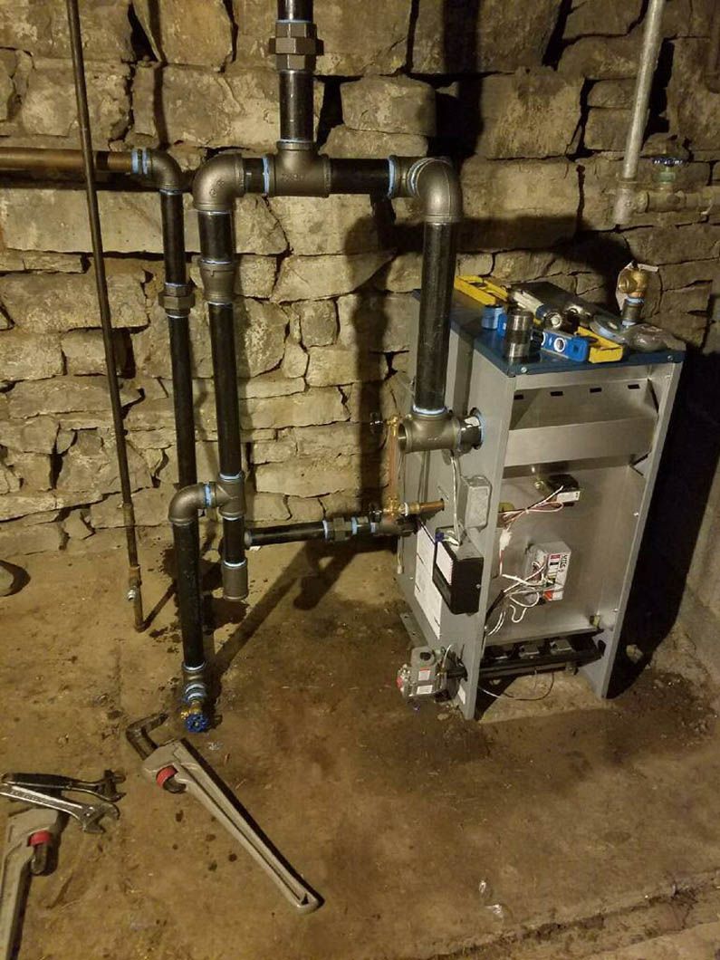 Basement utility area with exposed pipes, a boiler unit, and tools on the floor against stone walls