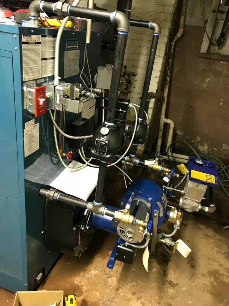 Industrial boiler room with blue pump, black tanks, and metal pipes on a wet floor.