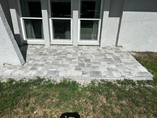 A gray and white stone paver patio situated outside a home with three glass sliding doors and textured light walls. A gray and white stone paver patio situated outside a home with three glass sliding doors and textured light walls.