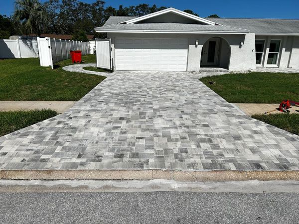 A white house with a large, newly installed grey paver driveway extending from the street to the garage. A white house with a large, newly installed grey paver driveway extending from the street to the garage.