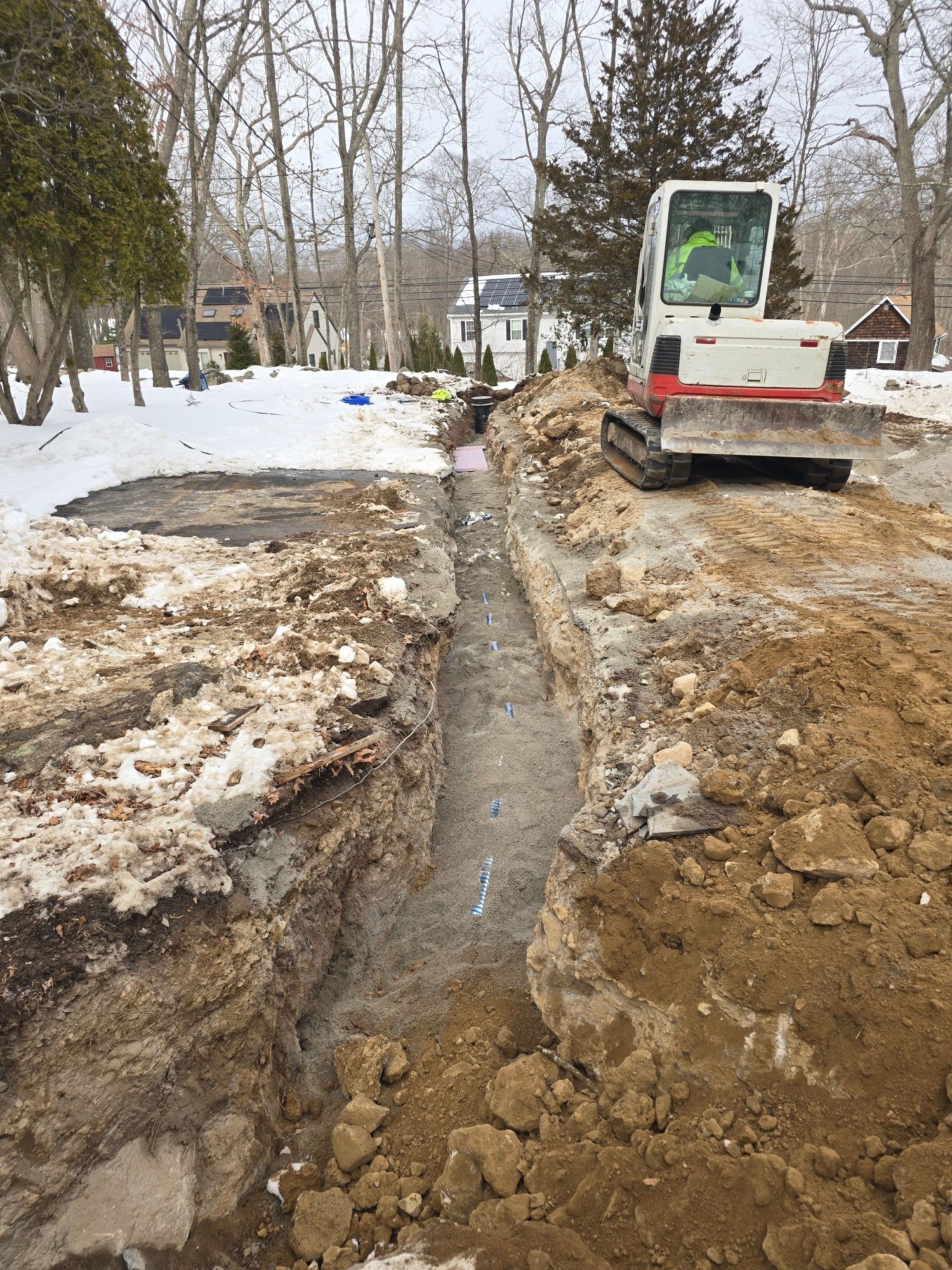 An excavator and trench in a snowy area, possibly for utility work.