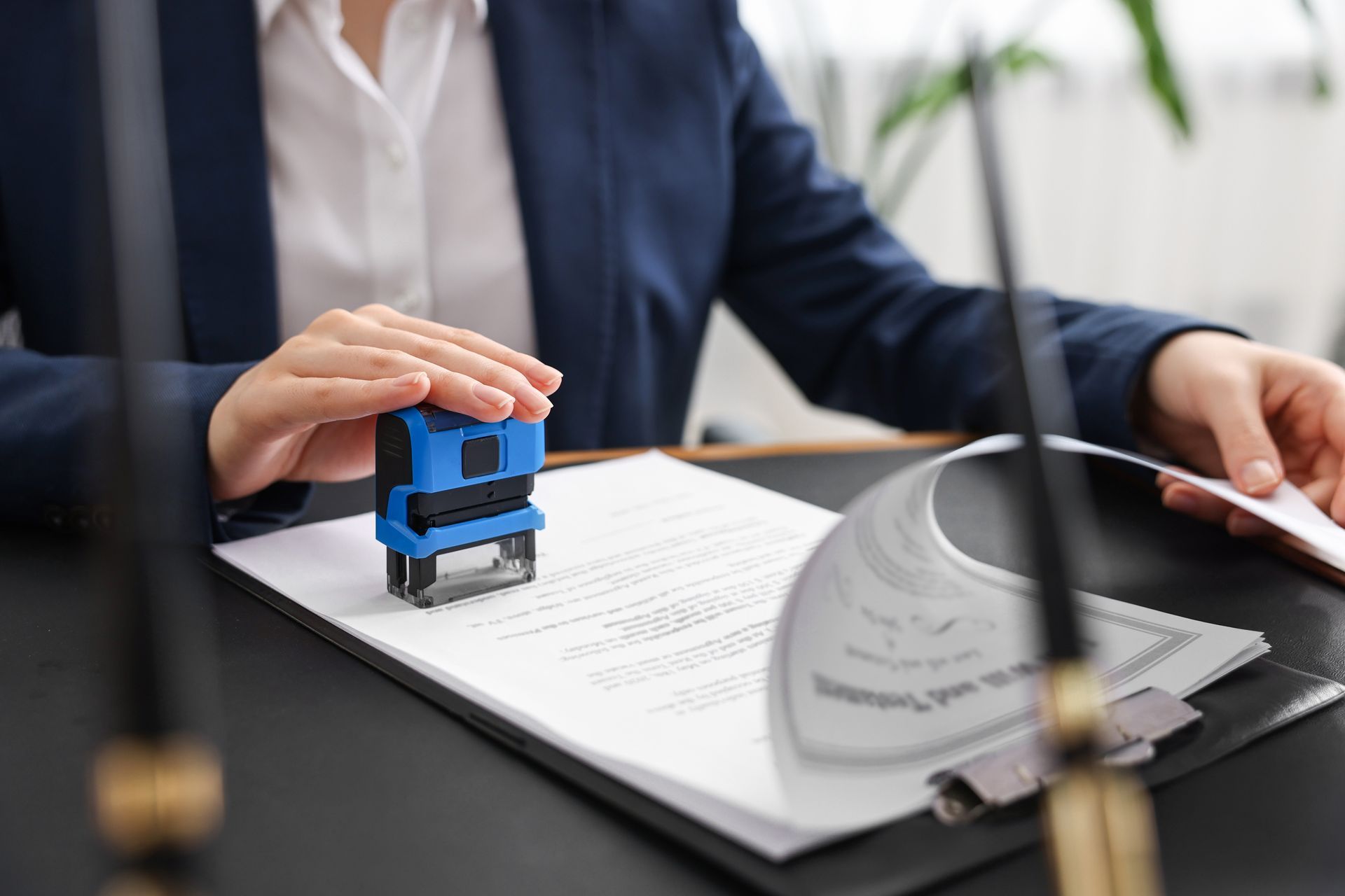 Person in a suit stamping a document with a blue stamp at a desk.